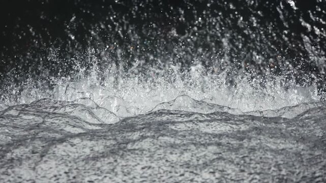 Water splashes dynamically as waves crash against the surface, showcasing the fluid motion and energy, with camera following the action through a gradual zoom in