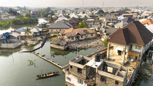 Aerial view of houses standing on the edge of the water, their decaying walls reflecting in the still water, a small boat adrift, Bolo Town, Rivers State, Nigeria