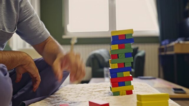 A captivating close-up of a person's hands delicately balancing and stacking colorful wooden blocks to build a tower. Enjoy the immersive sounds of the game play.