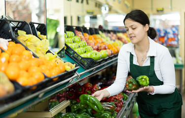 Positive asian girl seller in an apron offers fresh green bell peppers