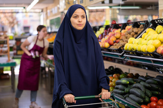 Portrait of young woman in veil, walking with a shopper cart, making the necessary purchases