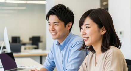 Young professional colleagues share a positive moment while working at their desks in a modern office setting.