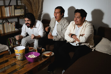 Two friends cheering while one calmly observes during TV event