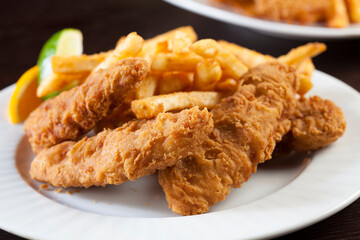 Fried fish and chips on a white plate with a dark background. 