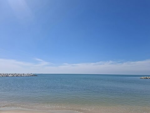The image depicts a calm seaside scene with gentle waves lapping against a sandy shore. The water is a clear shade of blue green, gradually darkening as it extends toward the horizon.