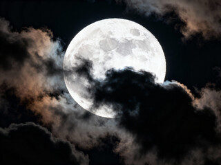 a full moon is seen through dark clouds, with the bright light of the moon contrasting against the black sky.