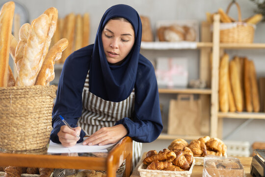 European Muslim woman in a hijab checks the order and fills out documents on the availability of goods. Owner of the bakery arranges deliveries and accepts wholesale orders