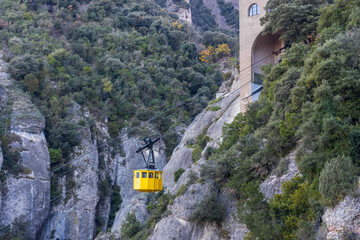 Yellow cable car is suspended above a rocky mountain
