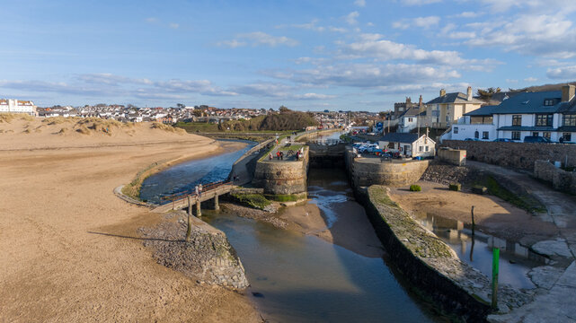 Aerial view of the serene canal meeting the sandy beach under a bright sky, with buildings nestled along the coast, Bude, England, United Kingdom. - Powered by Adobe