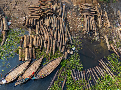 Aerial view of logs and boats clustered by the riverbank, creating a textured tableau of wood and water lilies, Floating Wood market, Dhaka Division, Bangladesh.