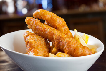 Large crunchy fish and chips on a white plate with dark background. 
