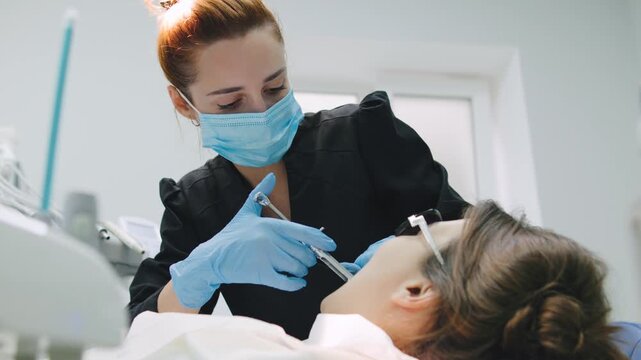 A dentist wearing gloves and a mask carefully and meticulously examines the patient's teeth and administers an anesthetic injection in a modern dental office equipped with all the necessary equipment.