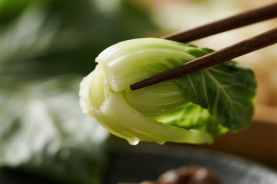 Chopsticks holding a fresh bok choy leaf with water droplets, close-up shot