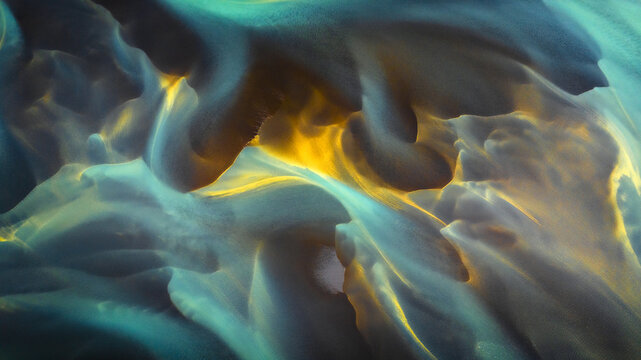 Aerial view of glacial river patterns display a mesmerizing swirl of turquoise, gold, and grey hues creating an ethereal landscape, Hvolsvollur, Rangarbing eystra, Iceland.
