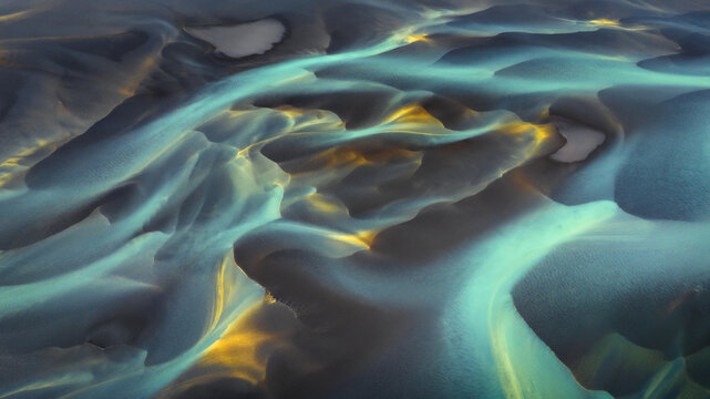 Aerial view of glacial rivers carve through the volcanic sands, a tapestry of turquoise and gold against the stark, grey landscape., Hvolsvollur, Rangarbing eystra, Iceland.