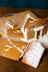 Vertical photo. Top view. Broken tasty brown gingerbread house with white icing decor, sugar powder on wood cut board on table. Concept of Christmas gift, Happy New Year, sweet food, winter holiday