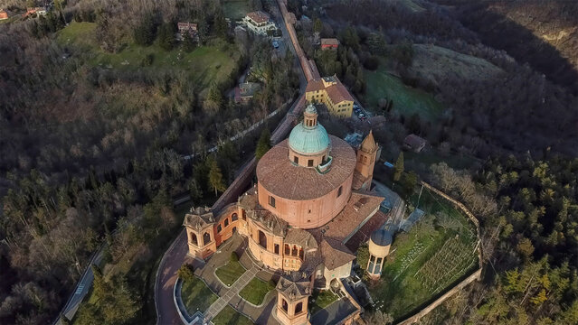 Aerial view of the Sanctuary of San Luca, a beacon of faith atop a hill, its terracotta hues contrasting with the emerald forests, Bologna, Emilia-Romagna, Italy.