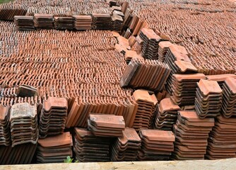A stack of clay roof tiles is placed in an open space. Traditional clay roof tiles.