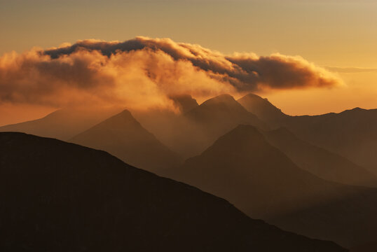 Aerial view of jagged peaks piercing through a sea of golden mist, crowned by a luminous cloud formation, Western Tatras, Jamnik, Zilina Region, Slovakia.