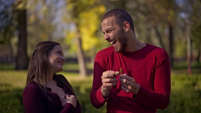 A beautiful young couple shares a happy and genuine moment of affection and communication in a vibrant green park on a sunny day, showcasing their loving relationship.