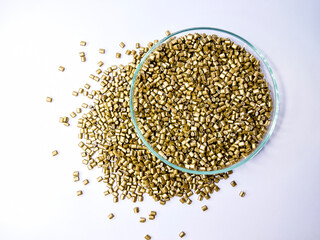 Gold masterbatch granules in a glass cup isolated on a white background, perfect for plastic industry company profile photo design, there is space for text.