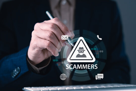 Scammers warning sign with hacker icon over businessman's hand holding pen and digital interface for online fraud and identity theft prevention concept