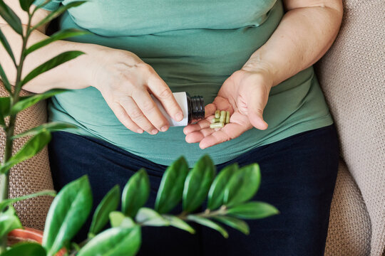 Mature woman with overweight pouring green capsules from bottle into her hand for daily health