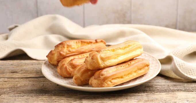 Woman taking tasty eclair from wooden table, closeup