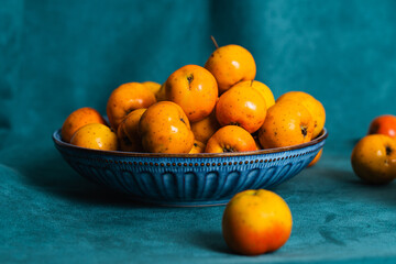 Ripe tejocotes filling a blue bowl on blue fabric