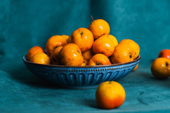 Ripe tejocotes filling a blue bowl on blue fabric
