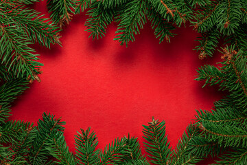 Frame of Christmas tree branches on red background with light and bokeh. Merry Christmas and Happy New Year greeting card. Xmas and Winter holidays. Christmas time, top view
