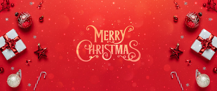 Merry Christmas gold text on red background with gift boxes, candy, red decoration bokeh, sparkles. Christmas and Happy New Year greeting card. Xmas and winter holidays, wide banner, top view