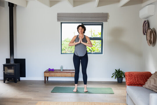 Woman practicing yoga in sportswear on green mat in home living room near bench with dumbbells