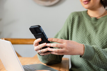 Smartphone being held while laptop is resting on wooden table in casual home workspace, copy space