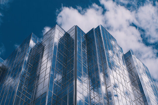 Modern glass skyscraper under a clear blue sky with clouds