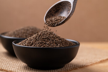 Dried perilla seed in spoon pouring into a bowl on brown background
