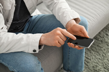 Young man with mobile phone messaging at home, closeup