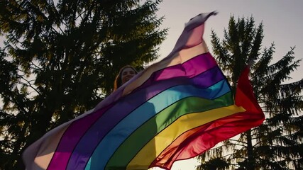A low-angle video shot of a colorful pride flag waving against a backdrop of tall trees, capturing a sense of freedom and diversity.