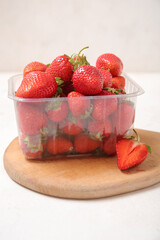 Plastic container with fresh strawberry and board on light background, closeup