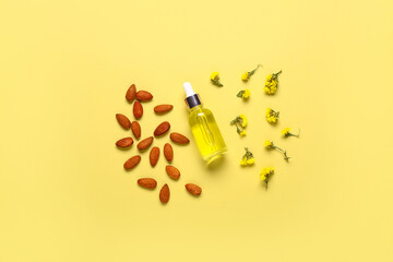 Bottle of cosmetic oil with almond and beautiful flowers on yellow background