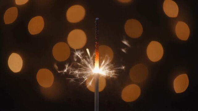 Bright festive sparkler ignites and sparkles with golden bokeh lights in dark