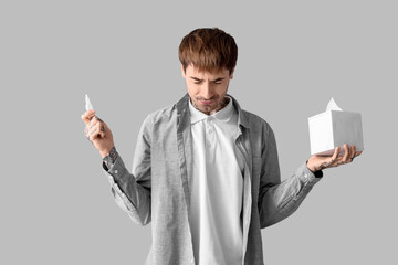 Allergic young man with nasal drops and tissues on grey background