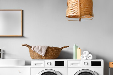 Interior of laundry room with washing machines, wicker basket and cleaning supplies