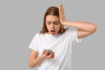 Fototapeta premium Shocked young woman reacting to bad news on smartphone, experiencing stress and disappointment, isolated on gray background