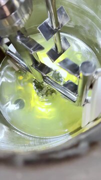 Close-up of an industrial mixer blending a golden liquid in a stainless steel tank, showcasing the precision and consistency of cosmetic or chemical production.