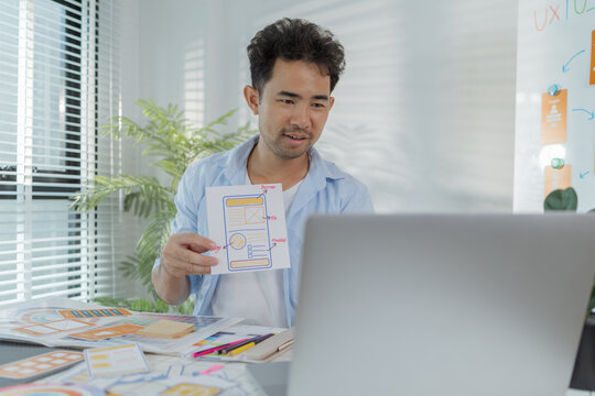 A focused designer is working on UX/UI design ideas, analyzing color palettes and interface structures pinned on a board. The scene reflects creativity, planning, and digital innovation.