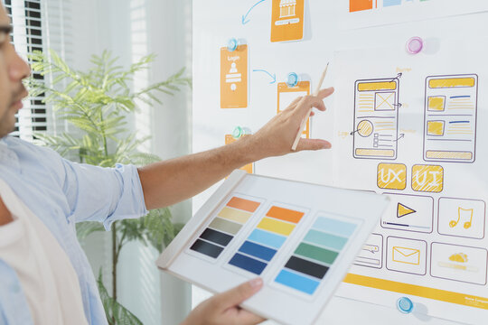 A young designer is working on a UX UI project, analyzing mobile app wireframes and choosing color palettes on a whiteboard. He focuses on brainstorming ideas to improve user experience.