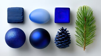 A collection of blue objects including a textured square, an oval, a glossy cube, two spherical ornaments, a pine cone, and a pine sprig, arranged on a white su