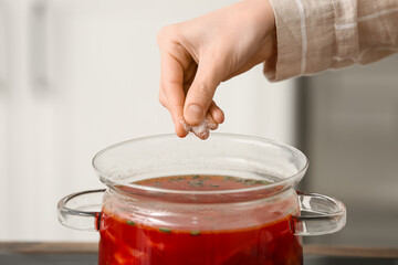Young woman salting delicious borscht in kitchen, closeup