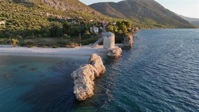 Greece,Kalamos Island,Agrapidia Beach,Aerial view half circle pan right around one and only standing windmill by the beach with sailboats anchored at the back ground.Early in the morning no people.